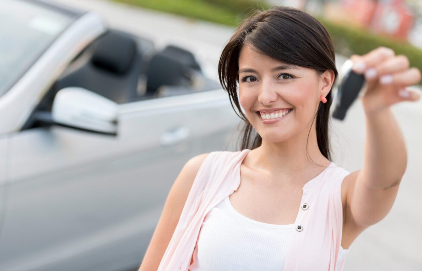 Young woman smiling while holding car keys in front of a white sedan